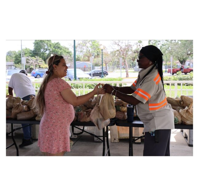 A Farm Share worker handing a bag of food to a woman at a distribution