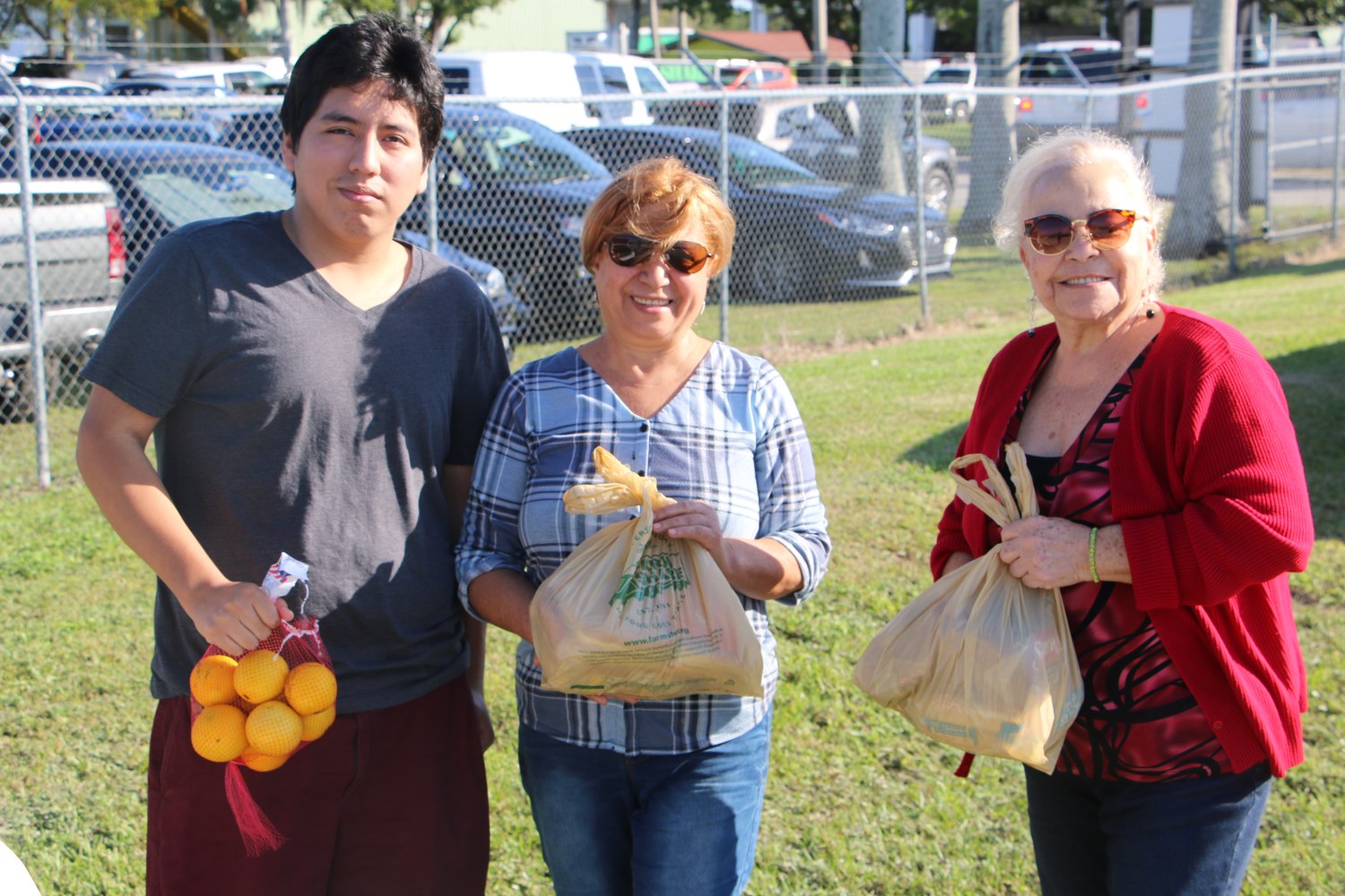 Three family members holding bags of fresh food at a Farm Share distribution