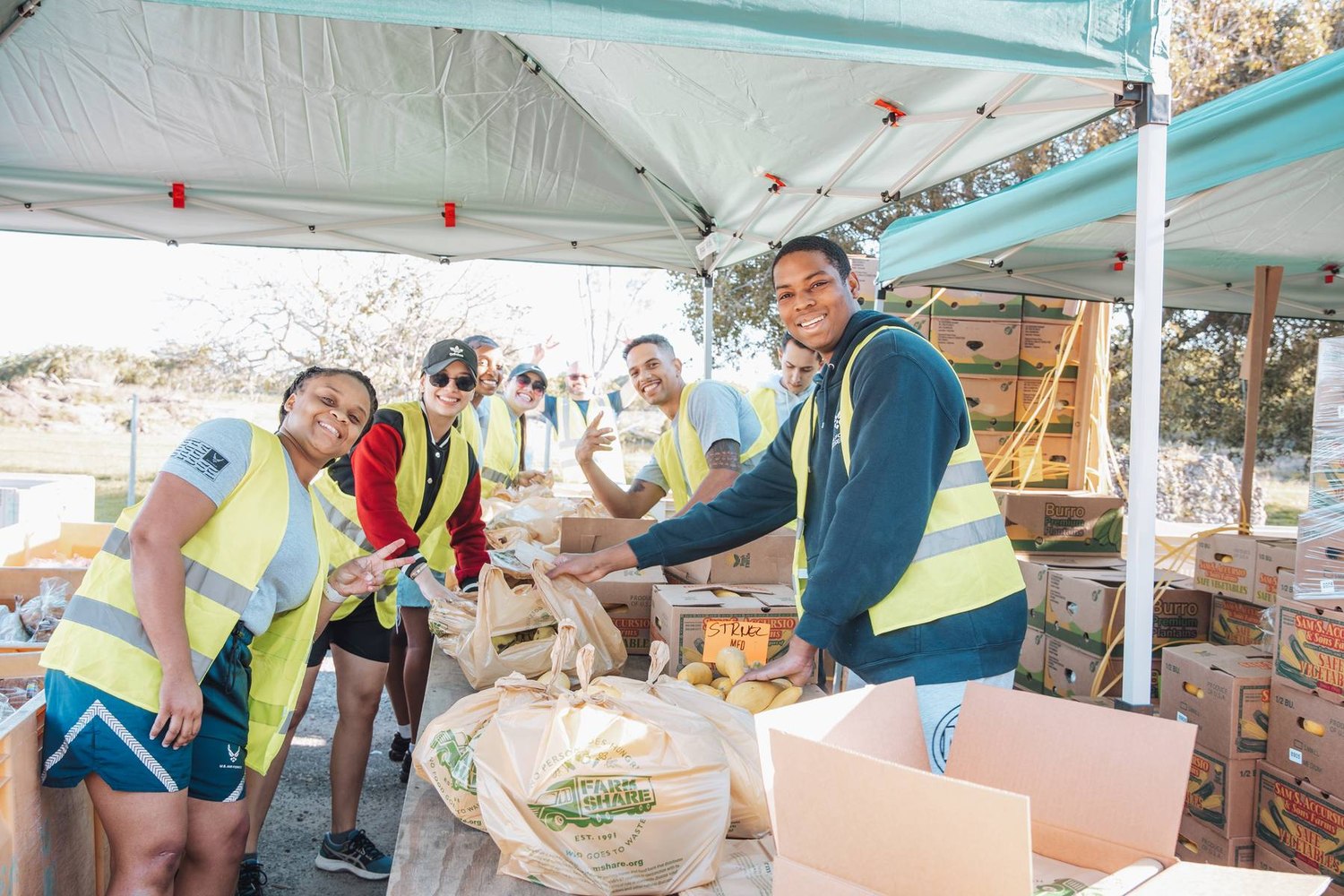 Volunteers in safety vests packing produce bags at a Farm Share distribution